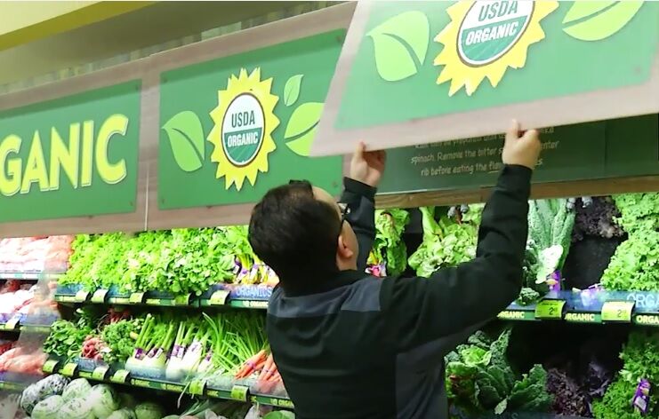 man taking down produce sign in grocer